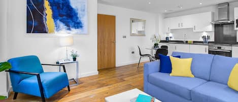 Un salon moderne avec un canapé bleu, une table basse sur laquelle sont posés des livres, un fauteuil bleu et un plancher en bois.