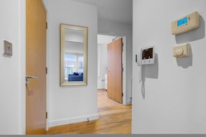 Un pasillo con una puerta de madera, un espejo enmarco y un termostato en la pared.