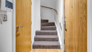 Eine Treppe mit Teppichstufen führt zu einer Zwischenebene, begleitet von Holztüren mit einem Sicherheitspanel auf der linken Seite.