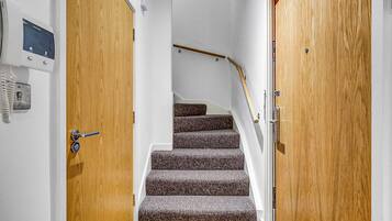 Eine Treppe mit Teppichstufen führt zu einer Zwischenebene, begleitet von Holztüren mit einem Sicherheitspanel auf der linken Seite.