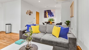 Ein modernes Wohnzimmer mit einem grauen Sofa, gelb-blauen Kissen, einem Couchtisch mit Pflanze und einem Gemälde an der Wand.