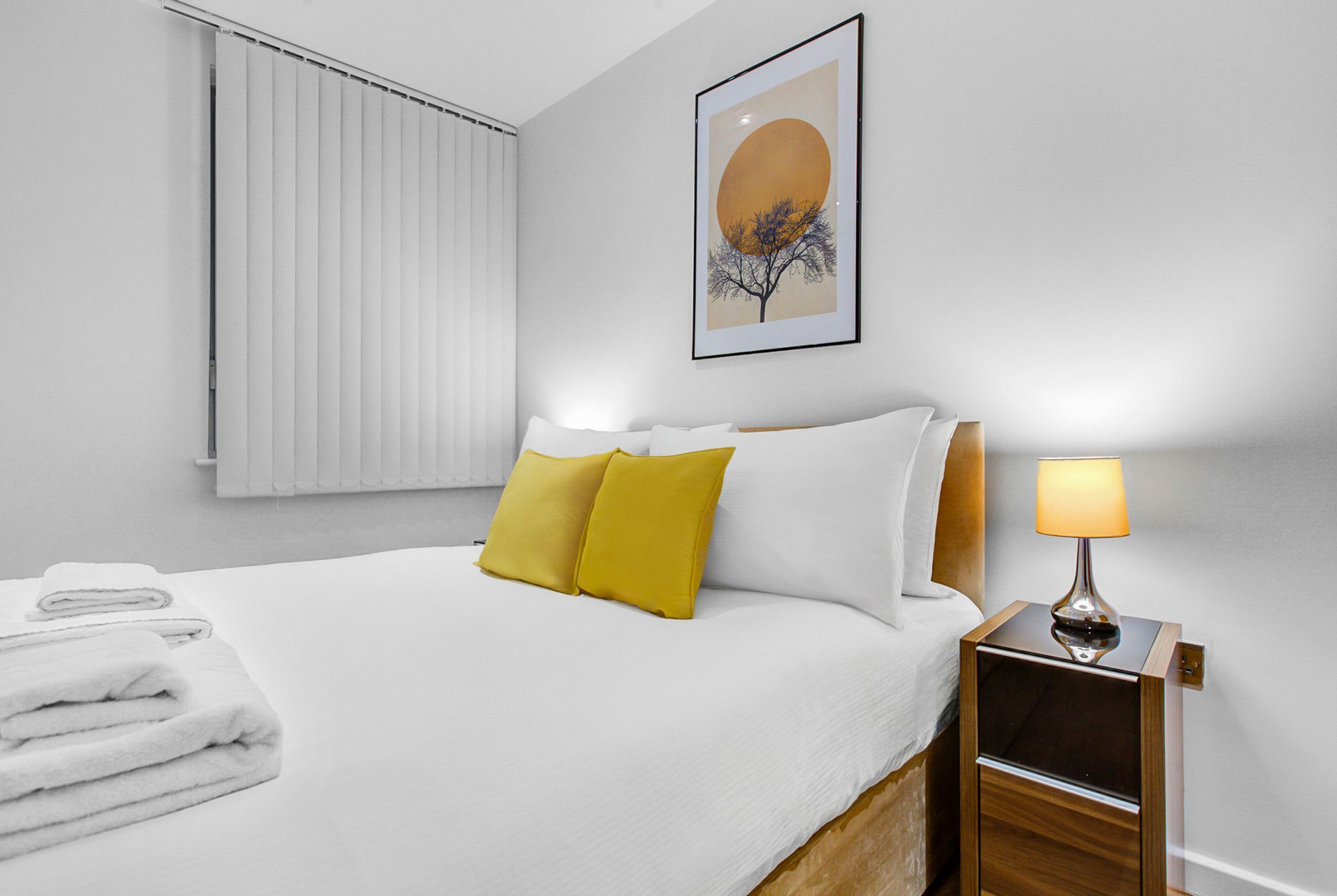 A hotel room with a neatly made bed, a bedside lamp, and a framed artwork on the wall.