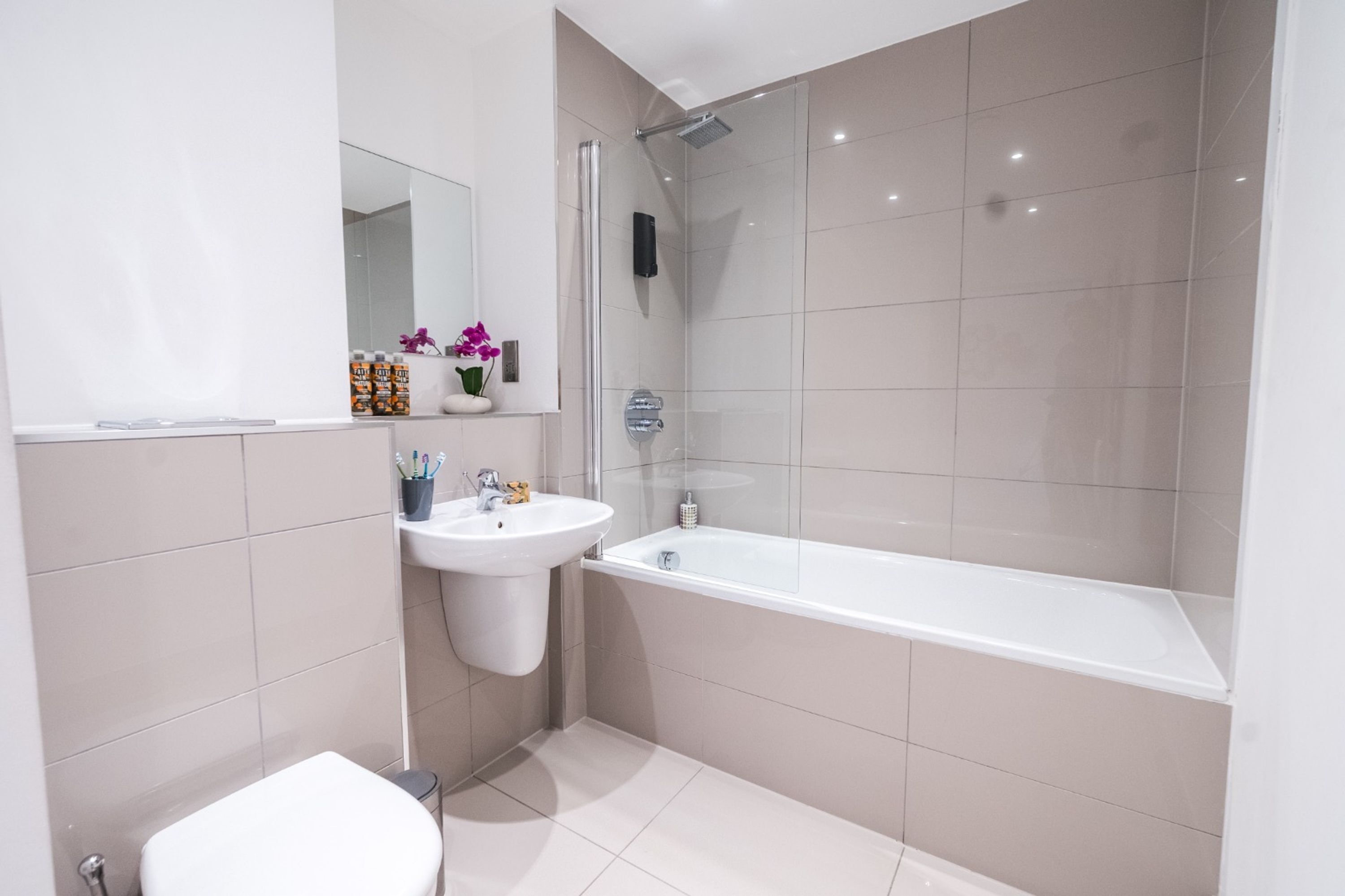 A modern bathroom with a white sink, mirror, and a glass-enclosed shower area.