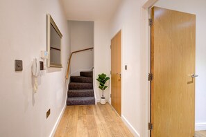A hallway with a wooden door, a staircase, and a potted plant. - Hybrid Resi - Greenwich - Three Bedroom Apartment (London)