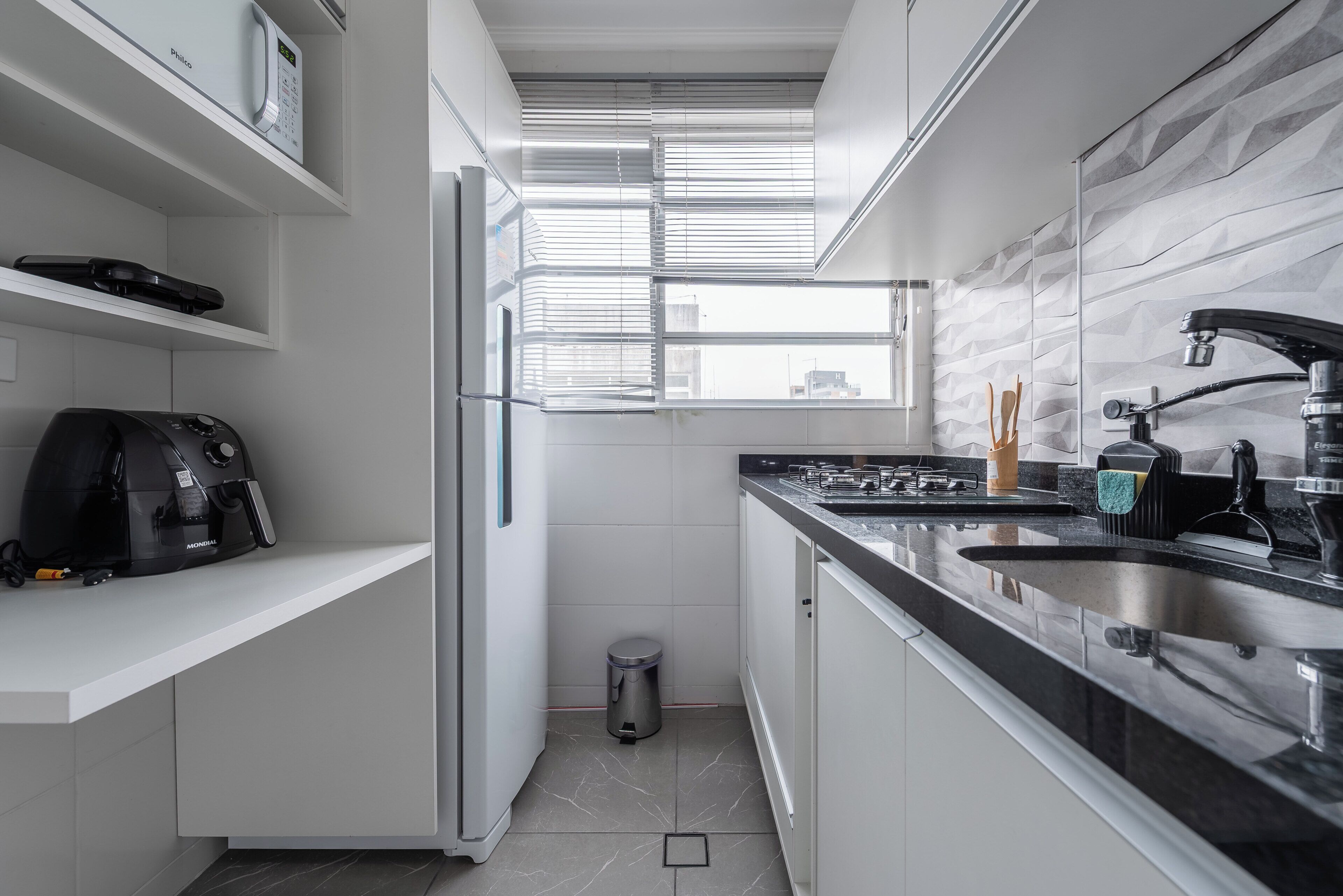 A modern kitchen with a built-in oven, a coffee machine, and a window with blinds.