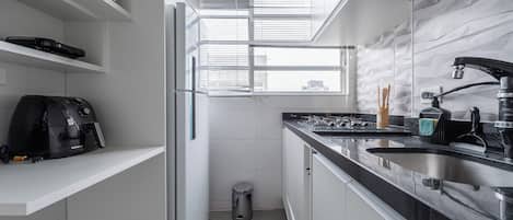 A modern kitchen with a built-in oven, a coffee machine, and a window with blinds.