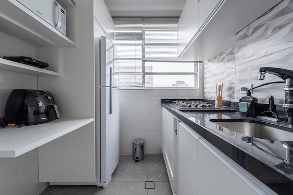 Una cocina moderna con horno empotrado, cafetera y ventana con persianas.
