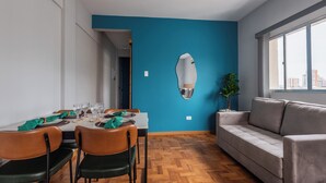 A modern dining area with a blue accent wall, wooden flooring, and a sofa.