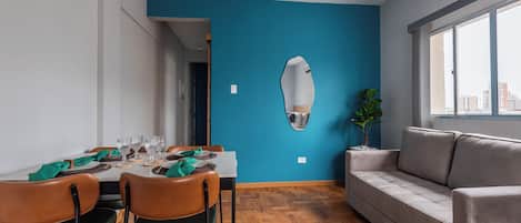 A modern dining area with a blue accent wall, wooden flooring, and a sofa.