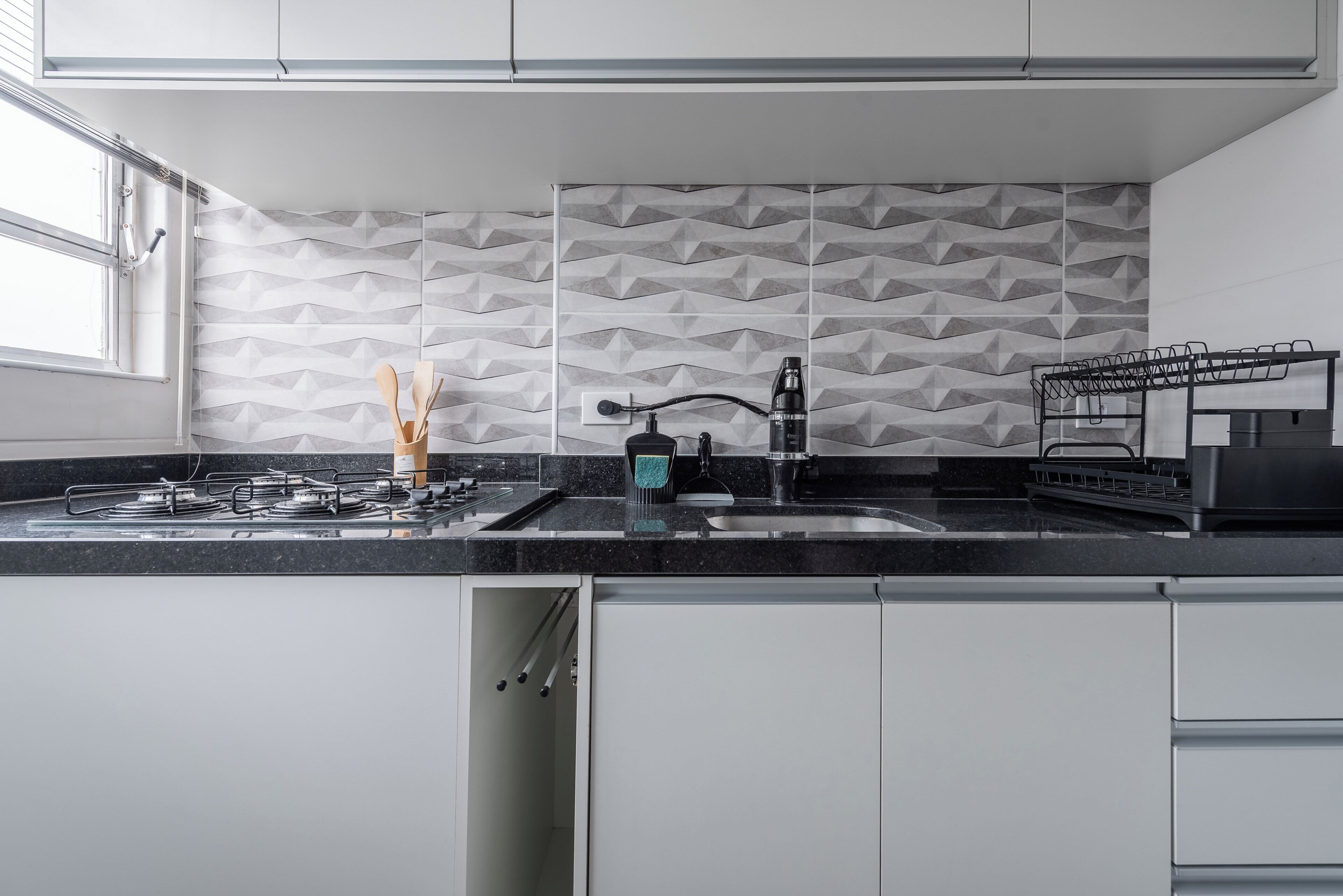 Una cocina moderna con estufa a gas, pileta y salpicadero con diseño geométrico.