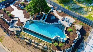 A swimming pool with a natural rock design, surrounded by a fence and landscaping. - Lux Lake View: Sleeps 12+, Hot Tub, Game Room, Theater, Fire Pit (Branson)