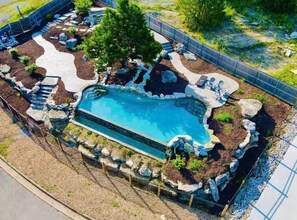 A swimming pool with a natural rock design, surrounded by a fence and landscaping. - Lux Lake View: Sleeps 12+, Hot Tub, Game Room, Theater, Fire Pit (Branson)