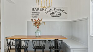 A kitchen with a wooden table, four black chairs, a vase with autumn leaves, and a wall sign advertising bakery items. - Lux Lake View: Sleeps 12+, Hot Tub, Game Room, Theater, Fire Pit (Branson)