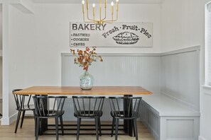 A kitchen with a wooden table, four black chairs, a vase with autumn leaves, and a wall sign advertising bakery items. - Lux Lake View: Sleeps 12+, Hot Tub, Game Room, Theater, Fire Pit (Branson)
