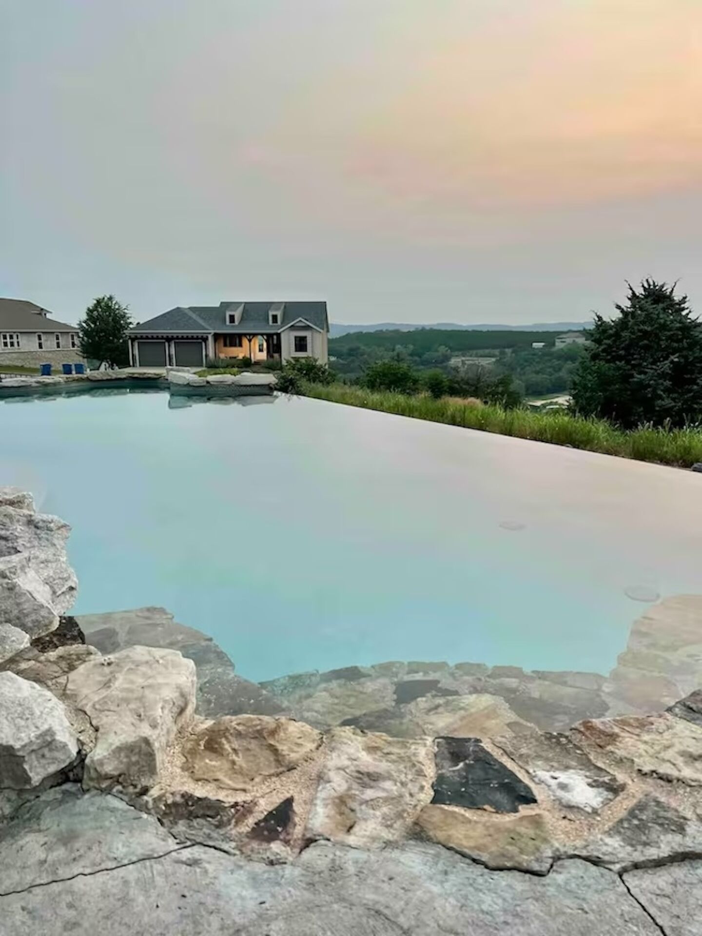Une piscine bordée de pierres, entourée d’une maison et de verdure.