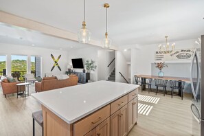 A modern kitchen with a large island, a dining area with a long table, and a living area with a sofa and chairs. - Lux Lake View: Sleeps 12+, Hot Tub, Game Room, Theater, Fire Pit (Branson)