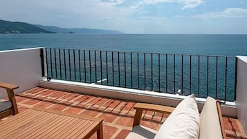 A balcony with a view of the sea, a wooden table, and a cushioned bench.