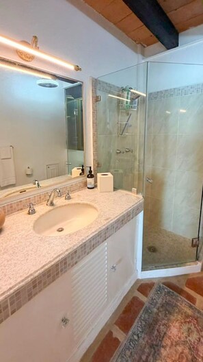 Ein Badezimmer mit Glasdusche, Waschbecken mit Spiegel und Handtuchhalter.
