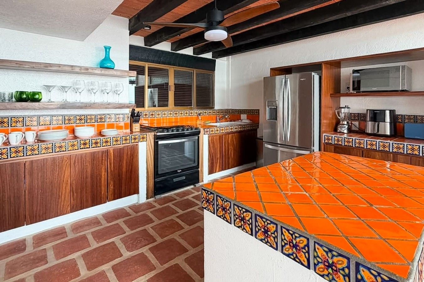 A kitchen with a tiled backsplash, wooden cabinets, a stainless steel refrigerator, and a brick floor.