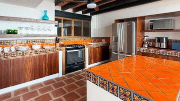 A kitchen with a tiled backsplash, wooden cabinets, a stainless steel refrigerator, and a brick floor.