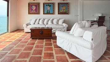 A room with a white sofa set, a wooden chest, and three colorful paintings on the wall.