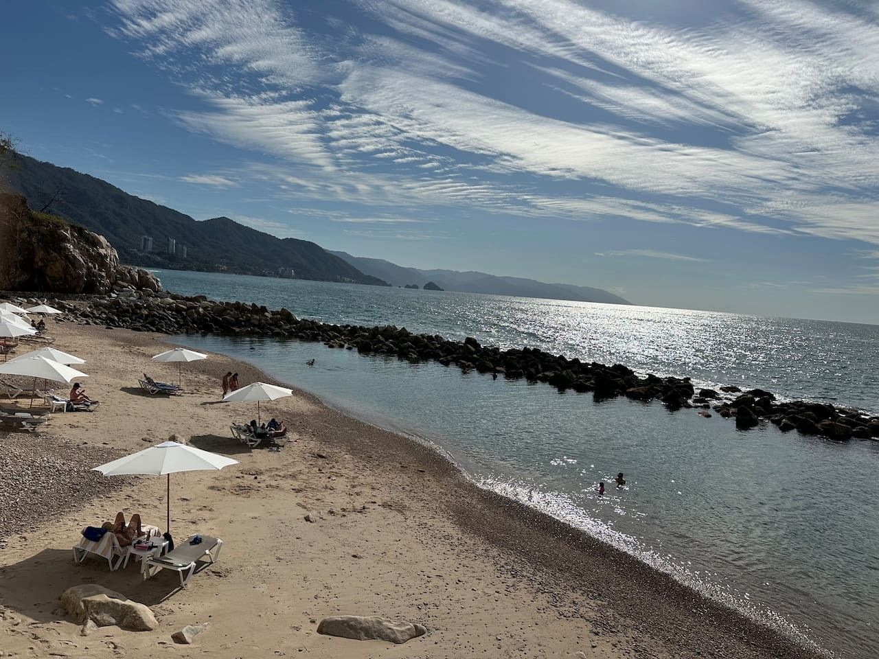 A beach with umbrellas, lounge chairs, and rocky shorelines.