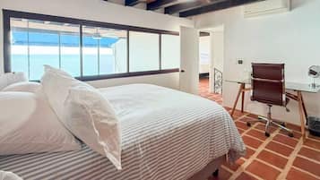 A hotel room with a large bed, a desk, and a view of the sea.