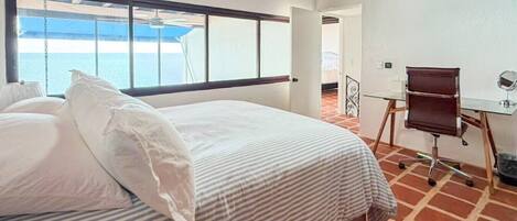 A hotel room with a large bed, a desk, and a view of the sea.