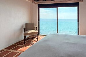 Ein Zimmer mit einem Bett, einem Sessel und einem großen Fenster mit Blick aufs Meer.