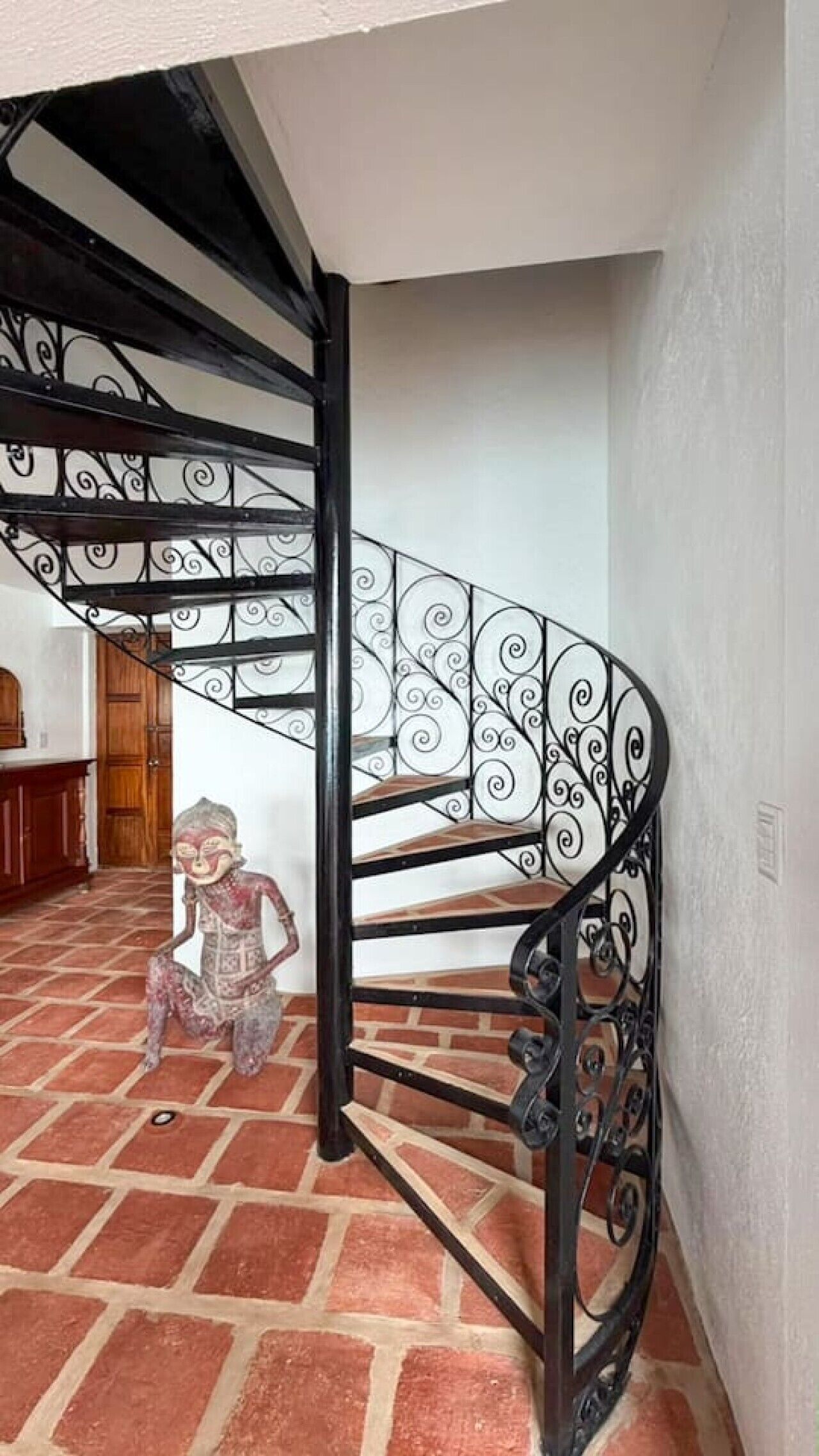 A spiral staircase with ornate metal railings and a brick floor.