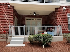 A building with a brick facade, a white balcony railing, and a small garden area with mulch and a bush.