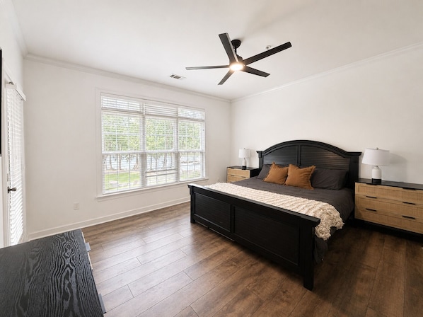 A bedroom with a dark wooden bed, white walls, a ceiling fan, and a window with blinds.