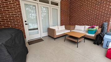 Ein überdachter Patio-Bereich mit Rattan-Sofa, einem kleinen Tisch und einem Grill mit Abdeckung.
