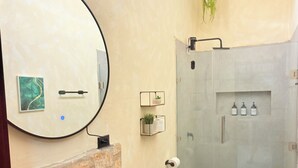 Een moderne badkamer met een ronde spiegel, een accentmuur van steen, een zwart wastafelbakje en een douchecabine met glazen wanden.