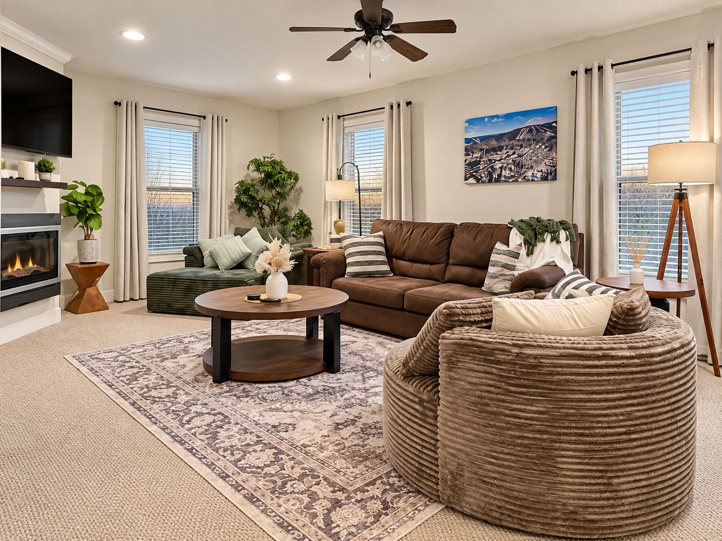 A living room with a fireplace, a ceiling fan, a large window with blinds, and a cityscape painting.