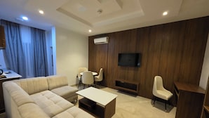 Una sala moderna con un sofá modular, una mesa de centro, un televisor montado en una pared de madera y un comedor con sillas.