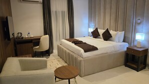 Habitación de hotel con cama, mesita de noche, escritorio, silla y una pequeña mesa redonda.
