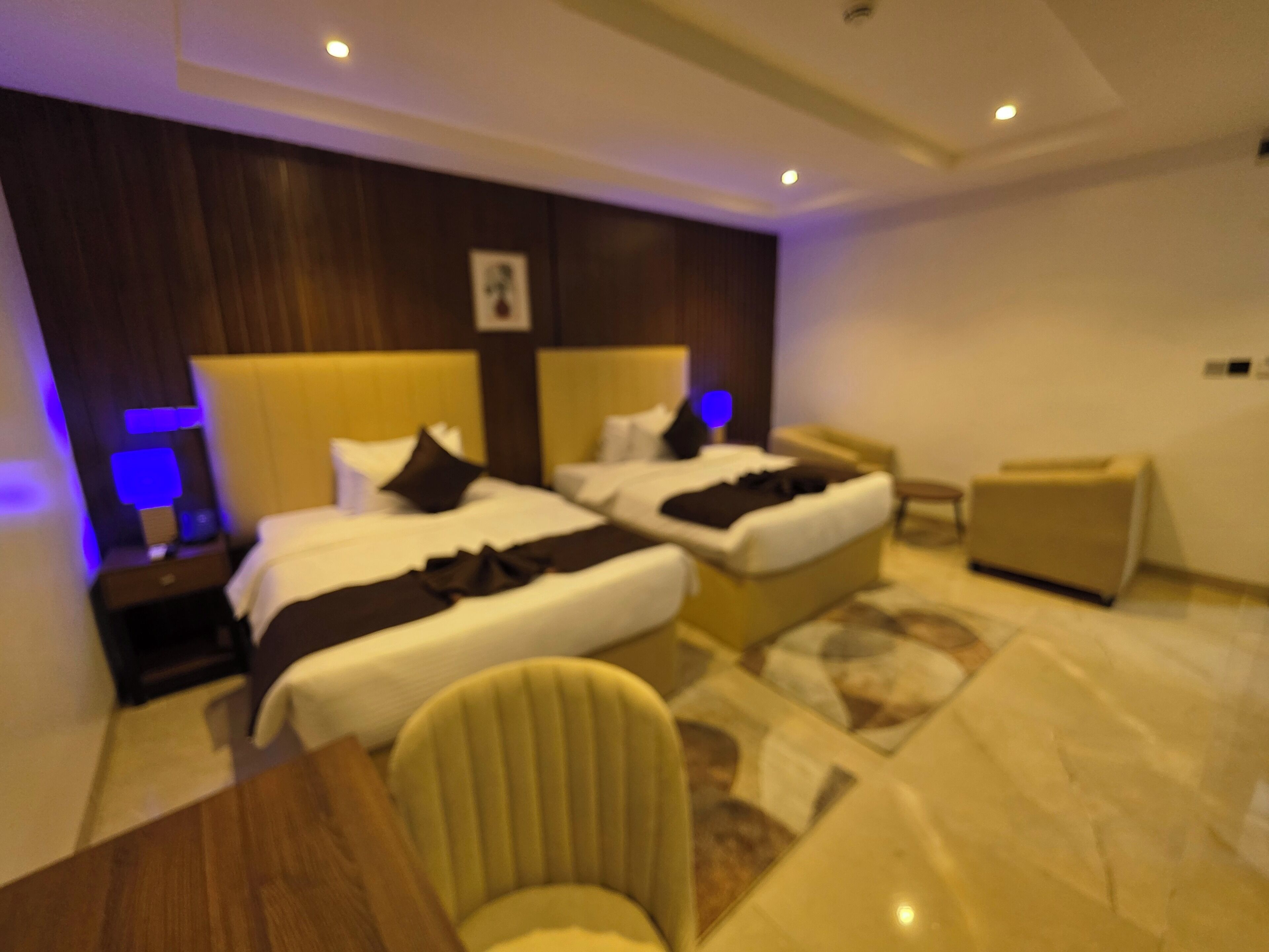 Habitación de hotel con dos camas, un sofá, una silla y una mesita de noche con lámpara.