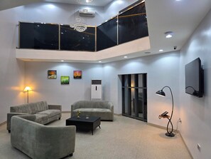 A modern living room with a high ceiling, two sofas, a coffee table, a floor lamp, and artwork on the walls.