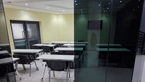 A classroom with tables and chairs, a door with a frosted glass panel, and a fire extinguisher on the wall.