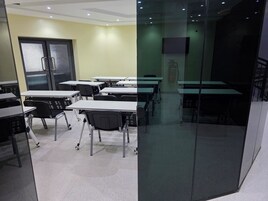 Un aula con mesas y sillas, una puerta con un panel de vidrio esmerilado y un extintor en la pared.
