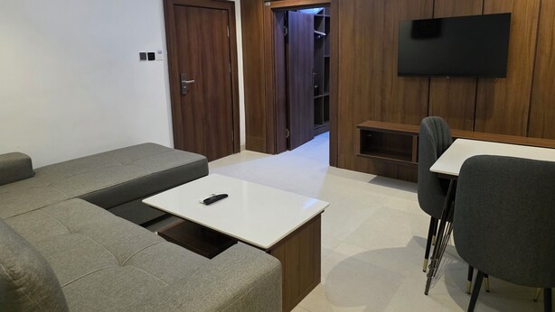 Una sala moderna con un sofá, una mesa de centro, un televisor montado en la pared y una pequeña mesa con una silla.