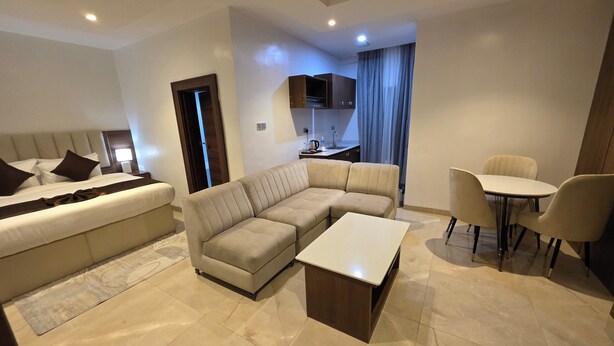 A modern living room with a sectional sofa, a small dining table, and a separate bedroom area with a bed.