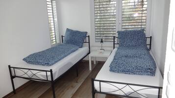 Une chambre avec deux lits simples, une petite table et une fenêtre avec des stores.