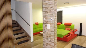 A modern interior with a staircase, wooden paneling, a green sofa set, and a wooden dining table.