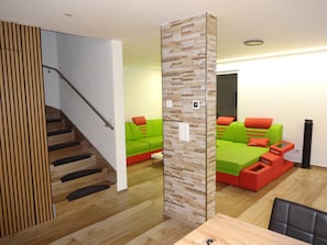A modern interior with a staircase, wooden paneling, a green sofa set, and a wooden dining table.