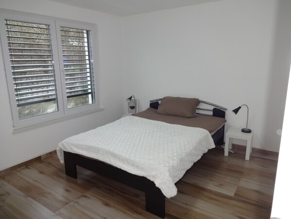 A bedroom with a bed, a nightstand, a lamp, and a window with blinds.