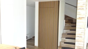 Un interior moderno con un separador de madera, una escalera de madera y un comedor con mesa y sillas.