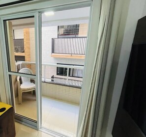 Un interior moderno con un ventanal corredero que da a un balcón con una silla blanca y una mesita.