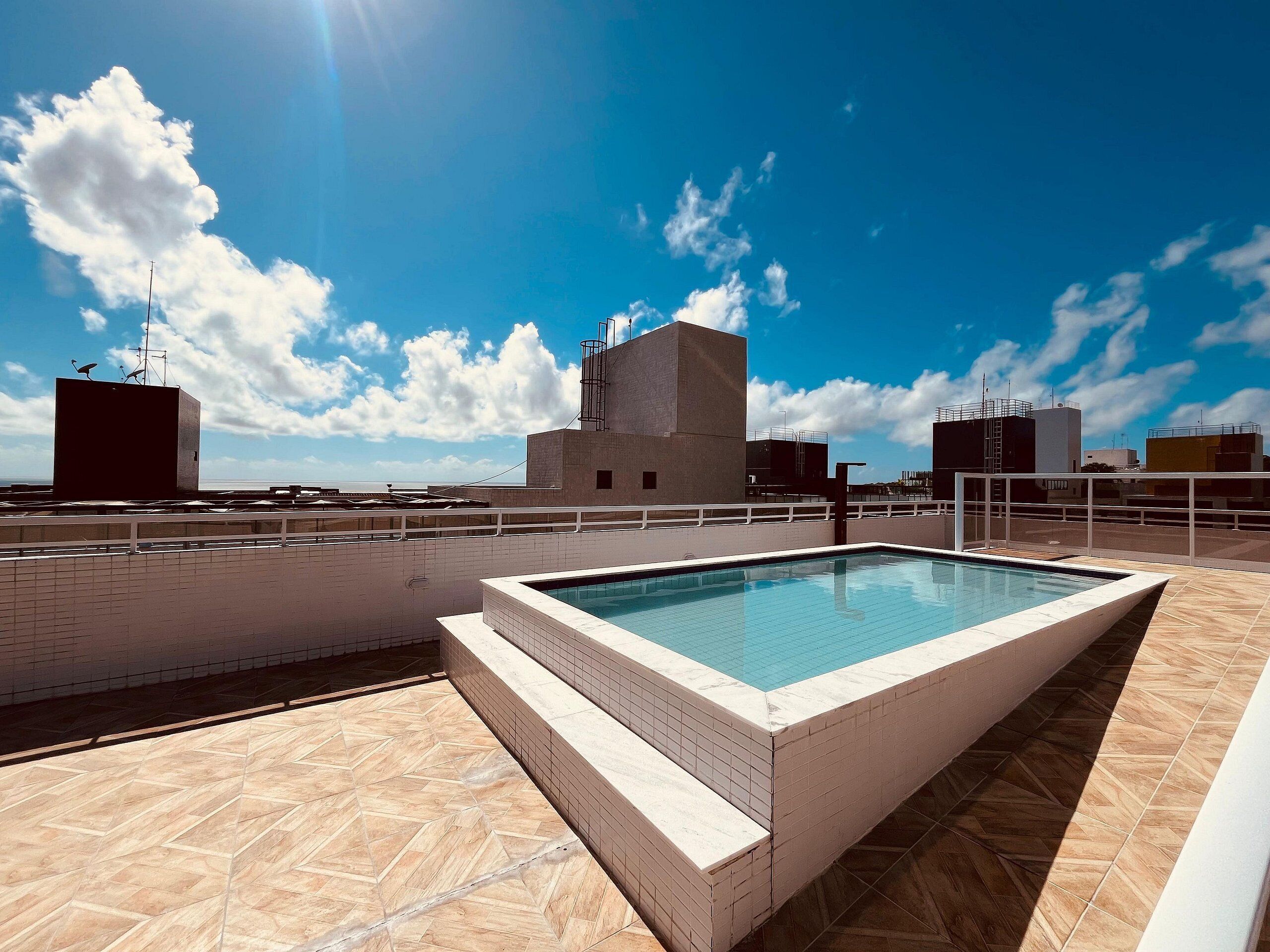 Una piscina en la azotea con vistas despejadas del horizonte urbano y un cielo azul.